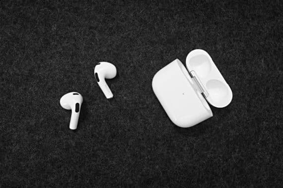 Weiße AirPods liegen neben einem geöffneten Ladecase auf dunklem Stoff.